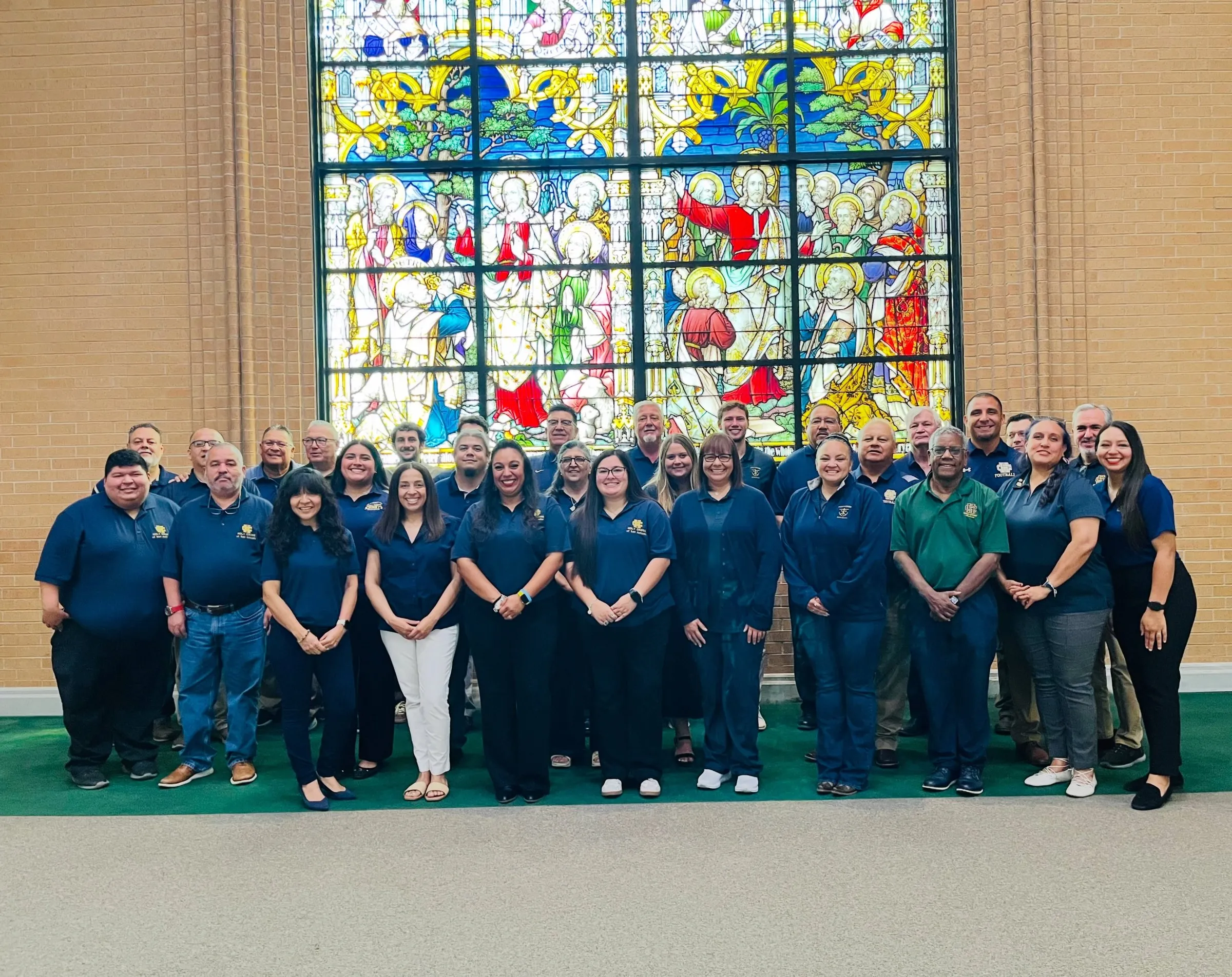 Holy Cross faculty and staff together in front of a large stained-glass window